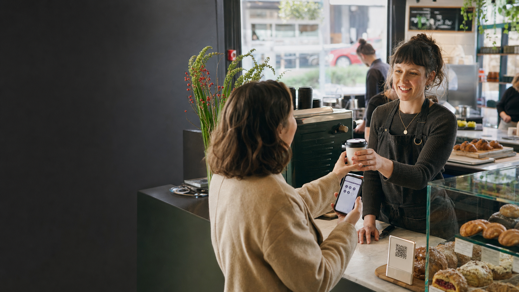 A cafe owner serving a returning customer who is using a digital loyalty card